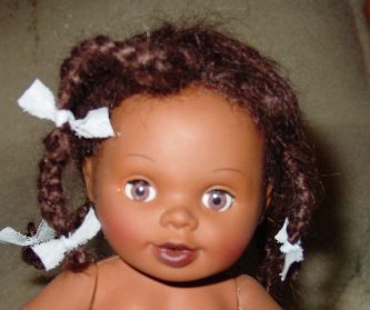 A brown-skinned doll with braided hair and a white bow.