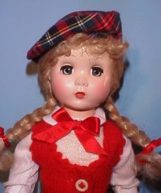 Vintage doll with braided hair wearing a red and white outfit and a plaid hat.