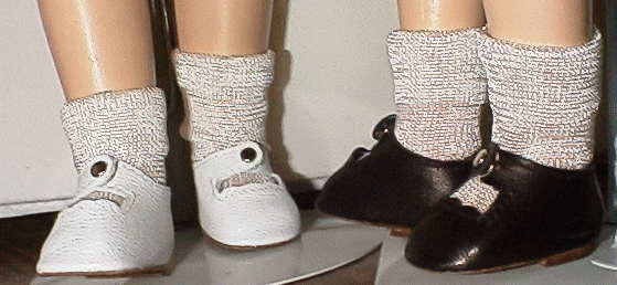 Two pairs of baby shoes on display stands with thick socks inside.